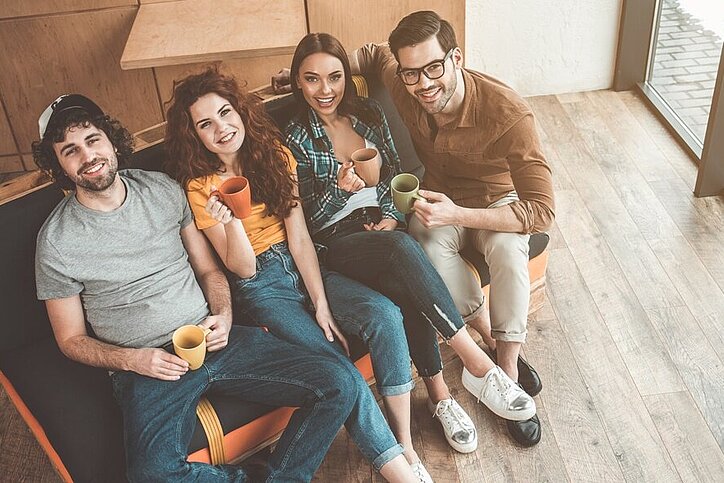 Echte Coliving-Angebote anbieten und finden – BookMyColiving will dem Markt einen Push verleihen. © AdobeStock_ Yakobchuk Olena Draufsicht auf fröhliche junge Männer und Frauen, die Tee trinken und auf dem Sofa sitzen. © AdobeStock_ Yakobchuk Olena